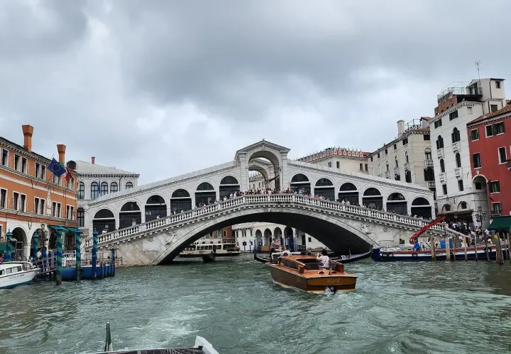 Un taxi venise navigue sur le Grand Canal, passant sous le célèbre pont du Rialto, bordé de bâtiments colorés.