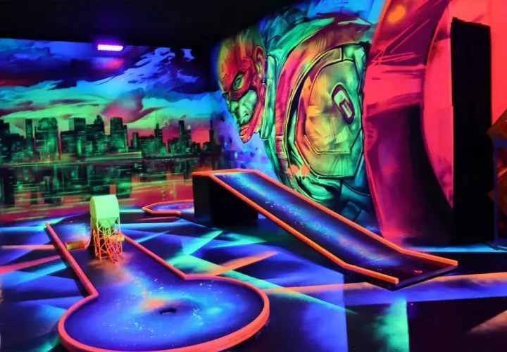 Neon-beleuchtete Bahnen und eine Skyline-Kulisse laden zum **Glow Minigolf** ein. Ein Superheld wacht über das Spiel.