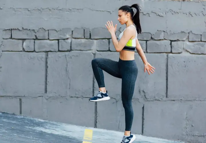 Kobieta wykonuje trening cardio w domu, podnosząc kolano do klatki piersiowej.