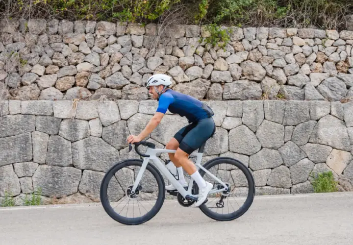 Ciclista pedaleando por una carretera en Mallorca en bici, con un muro de piedra detrás.