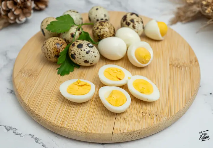 Huevos de codorniz cocidos y cortados por la mitad, mostrando sus yemas amarillas. Unos pocos huevos enteros y ramitas de perejil completan la escena.