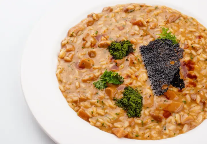 Risotto z grzybami i zieloną posypką na białym talerzu.
