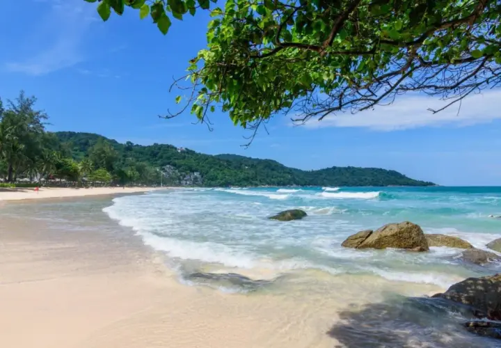 Piękna plaża Kata Beach z turkusową wodą, falami i zielonymi wzgórzami w tle.