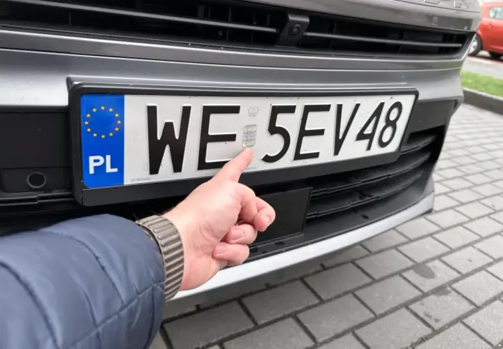 Palec wskazuje hologram na tablicy rejestracyjnej WE 5EV48, świeżo po rejestracji samochodu.