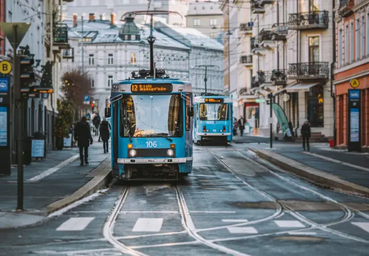 Niebieskie tramwaje na ulicy w Oslo, z budynkami po bokach.