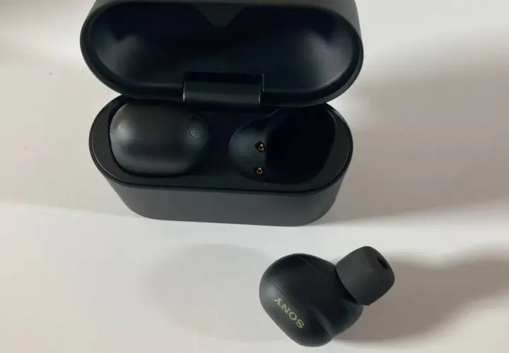Schwarze Sony WF-1000XM6 Kopfhörer mit Ladecase. Ein Ohrhörer liegt daneben.