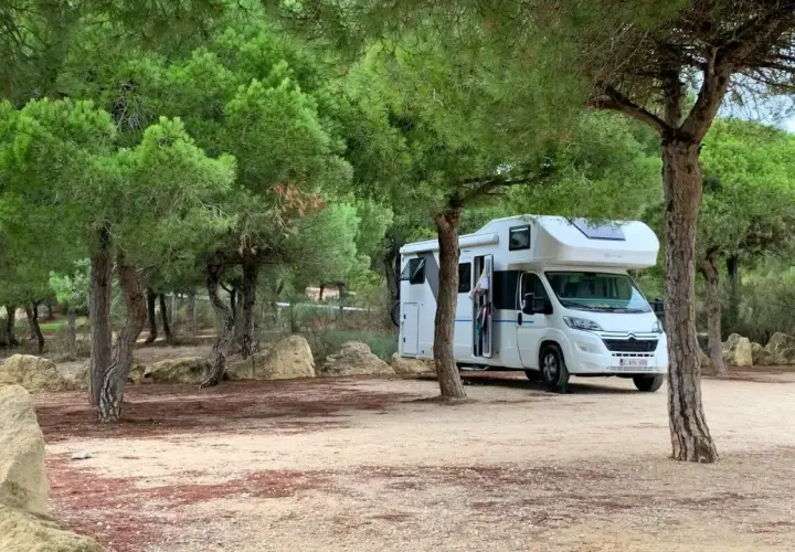 Un camping-car blanc est garé dans un endroit paisible, un spot camping-car sauvage, entouré de pins et de rochers.