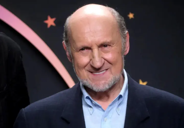 Uśmiechnięty Piotr Fronczewski, znany z wielu niezapomnianych ról w polskich filmach, na tle gwiazd.