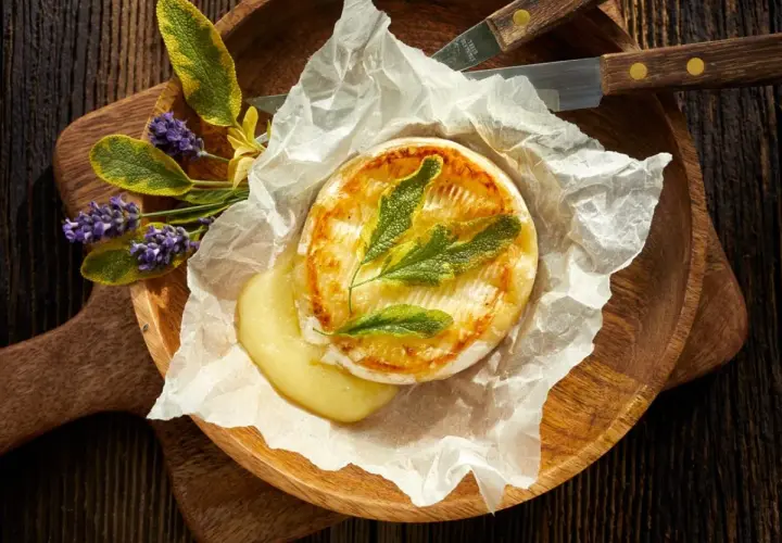 Camembert au barbecue, fondant et doré, servi sur papier sulfurisé avec des herbes aromatiques et des fleurs de lavande. Un délice à partager.