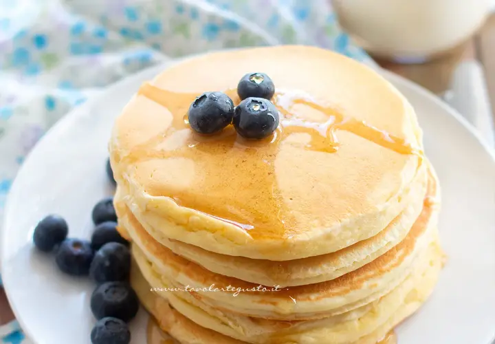 Pancake con albumi soffici e dorati, guarniti con mirtilli freschi e sciroppo d'acero.