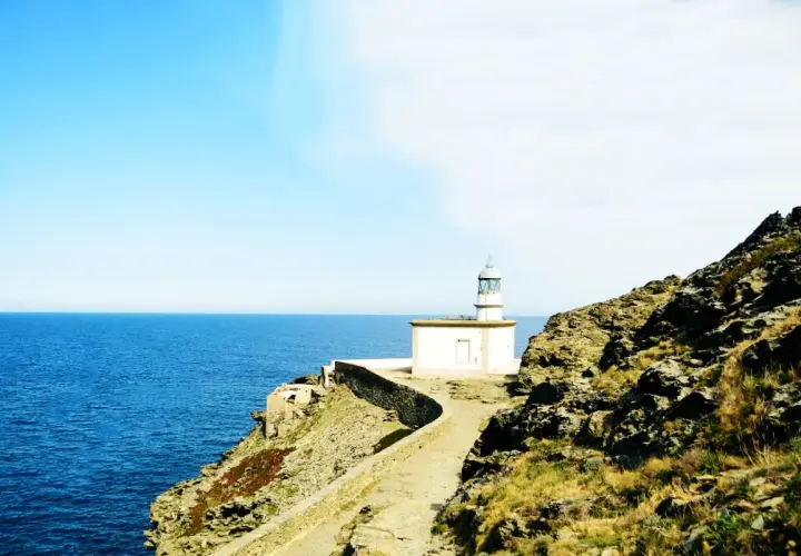El faro de Cala Nans se alza sobre un acantilado rocoso, vigilando el azul intenso del mar Mediterráneo bajo un cielo despejado.