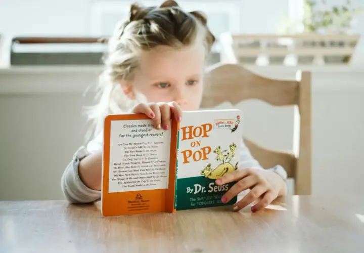 Dziewczynka czyta książki do czytania po angielsku, w tym "Hop on Pop" Dr. Seussa.