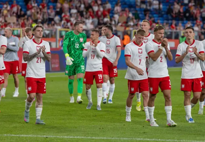 Piłkarze reprezentacji Polski w białych strojach z orzełkiem na piersi, klaskający na murawie. Ich pozycja w tabeli mistrzów Polski w piłce nożnej jest nieznana.