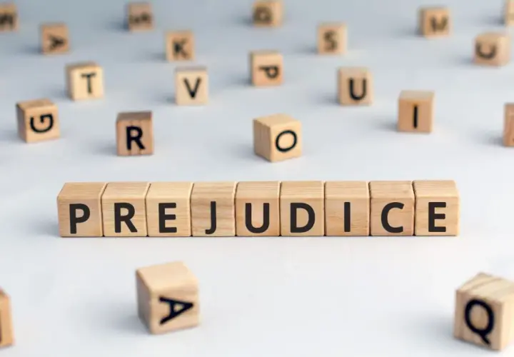 Des cubes en bois forment le mot "PREJUDICE", symbolisant le préjudice moral psychologique. D'autres lettres flottent autour.