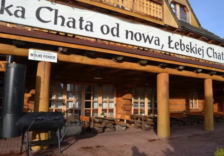 Drewniana, łebska chata z banerem "od nowa, Łebskiej Chaty". Przed wejściem grill i stoliki.