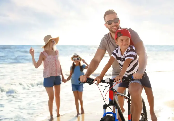Famiglia felice in bicicletta sulla spiaggia, un'idea per le tue prossime idee viaggio con bambini in Italia.