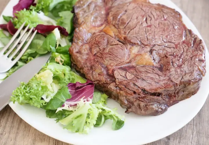 Un savoureux steak côté à l'os, accompagné d'une salade fraîche et colorée. Un délice prêt à être dégusté.