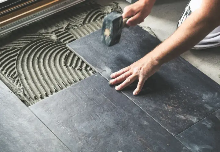 Mano che posa una piastrella scura su cemento fresco, con un martello per un posizionamento perfetto e rettificato.