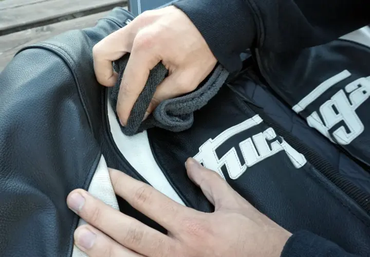 Manos limpian chaqueta de moto de cuero negro con detalles blancos. Aprende como lavar una chaqueta de moto.