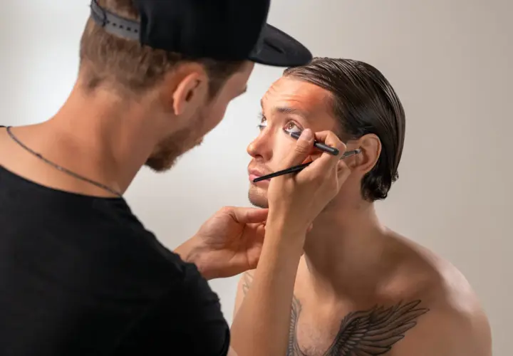 Un truccatore applica l'eyeliner a un modello, creando un look audace.