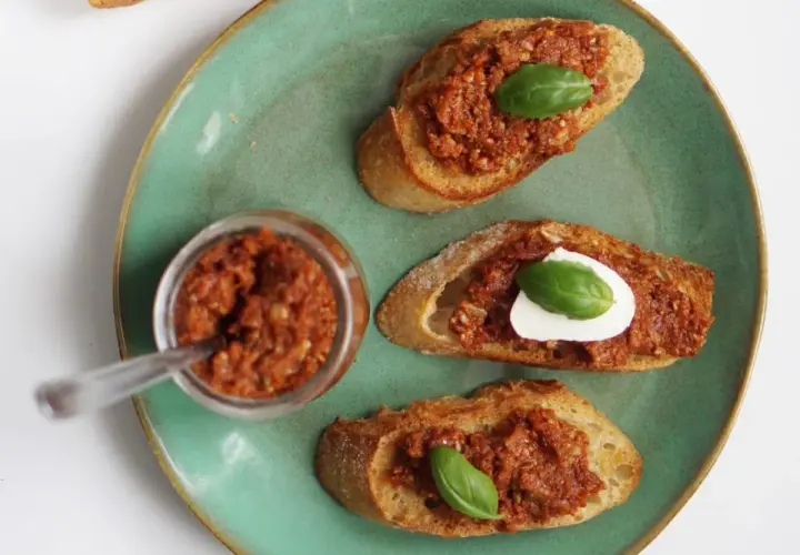 Chrupiące grzanki z aromatycznym pesto pomidorowym i listkiem bazylii. Obok słoiczek z pastą.