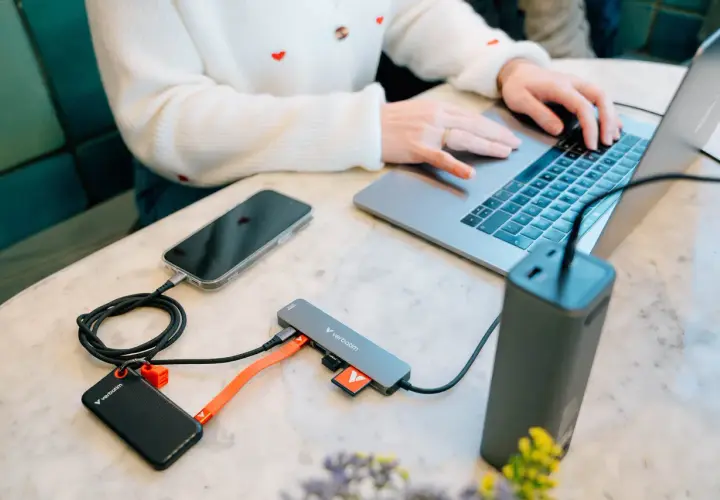 Kobieta pracuje na laptopie, podłączając telefon, dysk zewnętrzny i kartę SD do stacji dokującej USB 3.2.