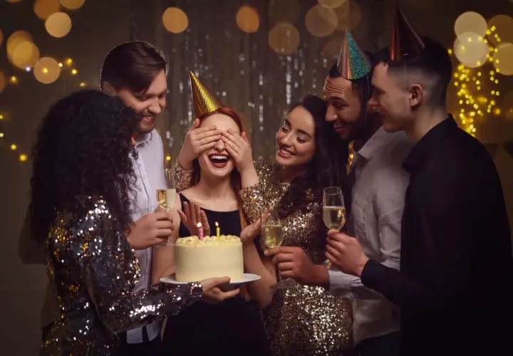 Grupa przyjaciół świętuje urodziny w domu. Jubilatka z zasłoniętymi oczami czeka na niespodziankę z tortem. To świetne, fajne atrakcje na urodziny w domu!