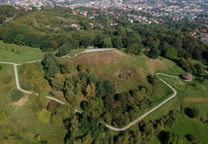 Widok z lotu ptaka na Kopiec Tatarski w Przemyślu, otoczony zielenią i wijącymi się ścieżkami. W oddali widać panoramę miasta.
