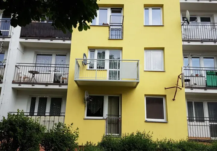 Żółty blok z balkonami. Widać, jak przedłużyć balkon betonowy, dodając nowoczesną, metalową konstrukcję.