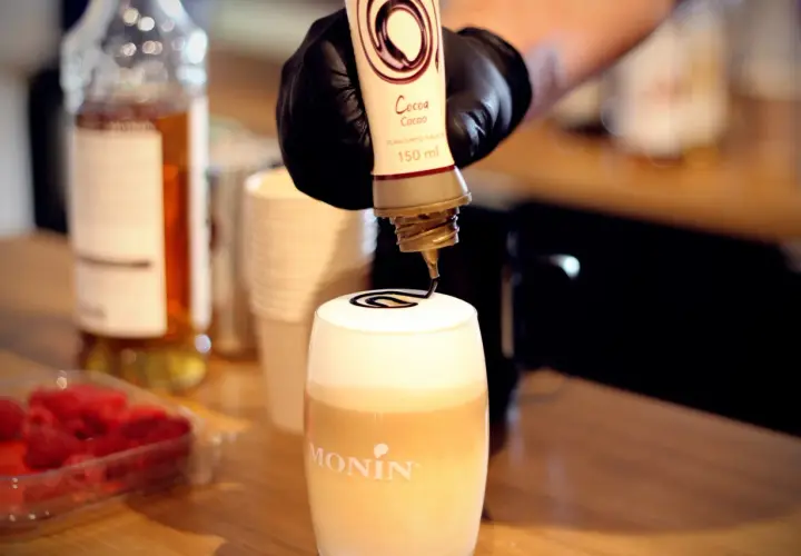 Barista ozdabia gorącą czekoladę do picia syropem kakaowym.