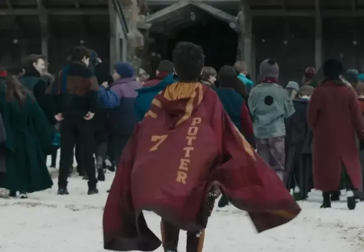 Chłopiec w pelerynie z napisem "POTTER 7" idzie przez śnieg w otoczeniu innych uczniów, jak w serialu Harry Potter.