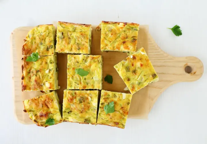 Pyszna frittata z cukinią pokrojona w kwadraty, ułożona na desce.