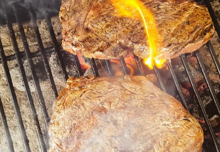 Två saftiga biffar grillas med ved. Flammor slickar köttet som får en perfekt yta.