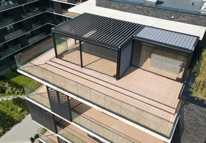 Nowoczesny taras na dachu z przeszklonym pawilonem i pergolą. Drewniana podłoga i szklane balustrady tworzą elegancką przestrzeń.