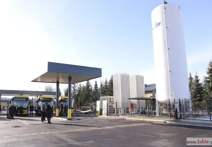 Stacja tankowania CNG. Żółte autobusy czekają pod wiatą, obok wysoki zbiornik i instalacja.