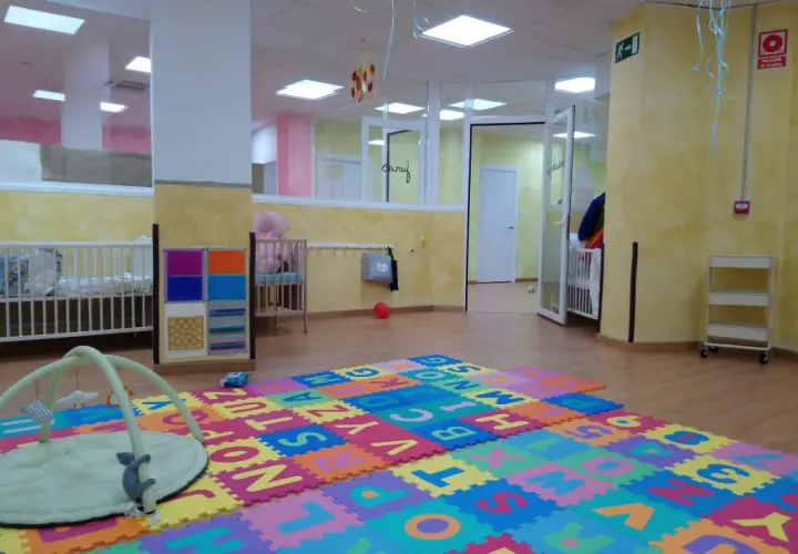 Un espacio acogedor en una escuela infantil o guardería, con cunas, alfombras de letras y juguetes para los más pequeños.