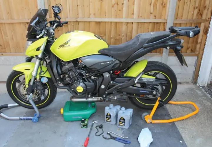 Moto Honda Hornet gialla pronta per cambiare l'olio di lubrificazione del motore. Attrezzi e olio a terra.