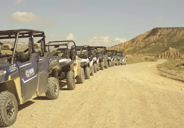 Una fila de vehículos todoterreno espera en un camino de tierra, listos para una aventura por el desierto, como si fueran un puente de todos los santos hacia lo desconocido.