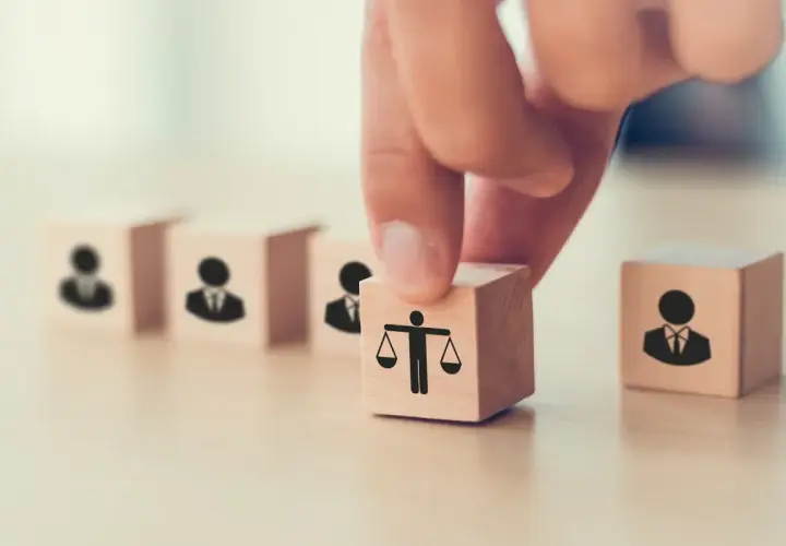 Dłoń układa kostkę z wagą sprawiedliwości obok kostek z ludzikami. To symbol tego, co daje członkostwo w partii: równość i reprezentację.