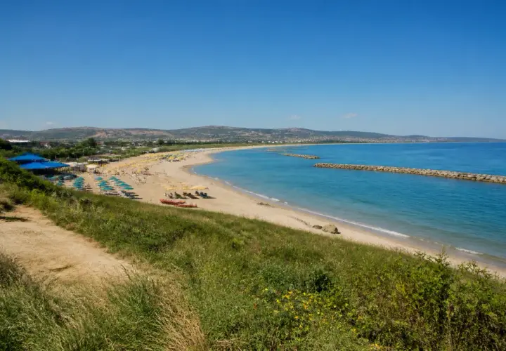 Plage de Pescara, Italie. Parasols bleus et jaunes, mer turquoise, digues en pierre, collines verdoyantes.