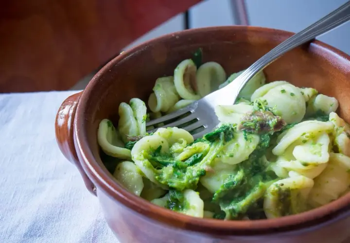 Orecchiette con cime di rapa, uno dei piatti tipici foggiani, servite in una ciotola di terracotta con una forchetta.