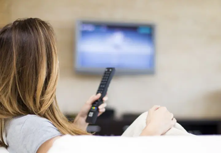 Kobieta z pilotem w ręku ogląda telewizję, ciesząc się swoim abonamentem radiowo-telewizyjnym.