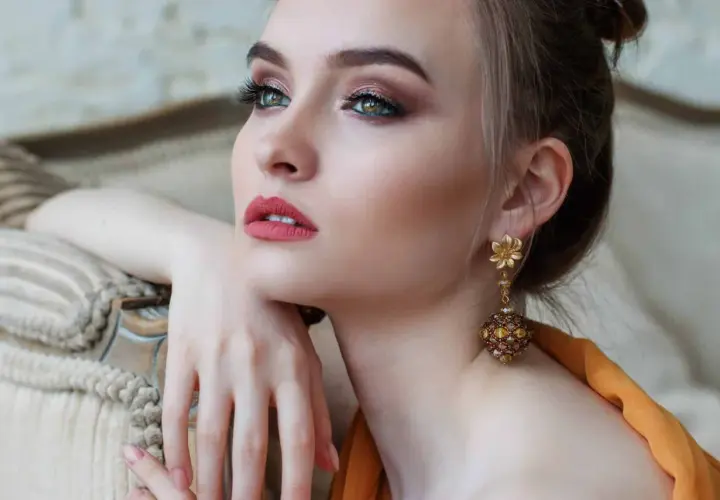Donna con elegante trucco semplice, labbra rosse e orecchini pendenti dorati.