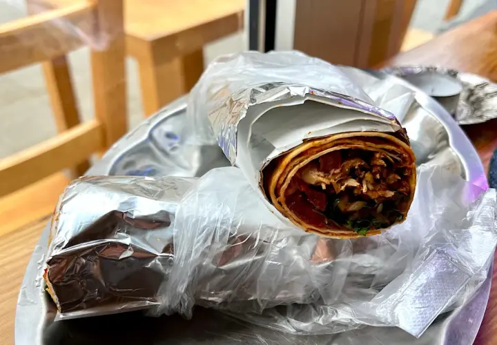 Dwa zawinięte w folię aluminiową i folię spożywczą tureckie wrapy z mięsem i warzywami na talerzu.
