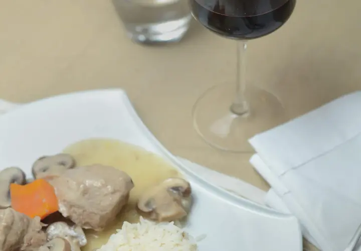 Un verre de vin rouge accompagne une blanquette de veau savoureuse avec riz et champignons.