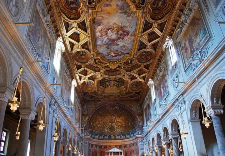 Intérieur de la basilique San Clemente à Rome, avec son plafond doré orné de fresques et ses arcs majestueux.