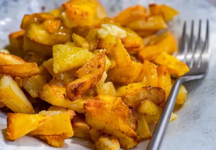 Un plato de papas al horno crujientes, doradas y sazonadas, listas para disfrutar con un tenedor.