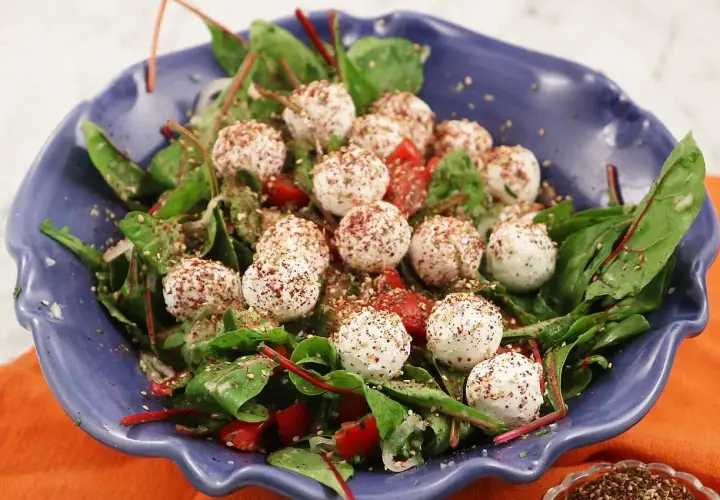 En blå skål med en sallad av gröna blad, körsbärstomater och små, kryddade labneh bollar.