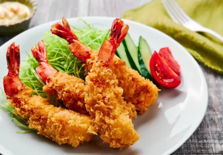 Crispy, golden japanese fried shrimp served on a bed of shredded cabbage with cucumber and tomato slices.