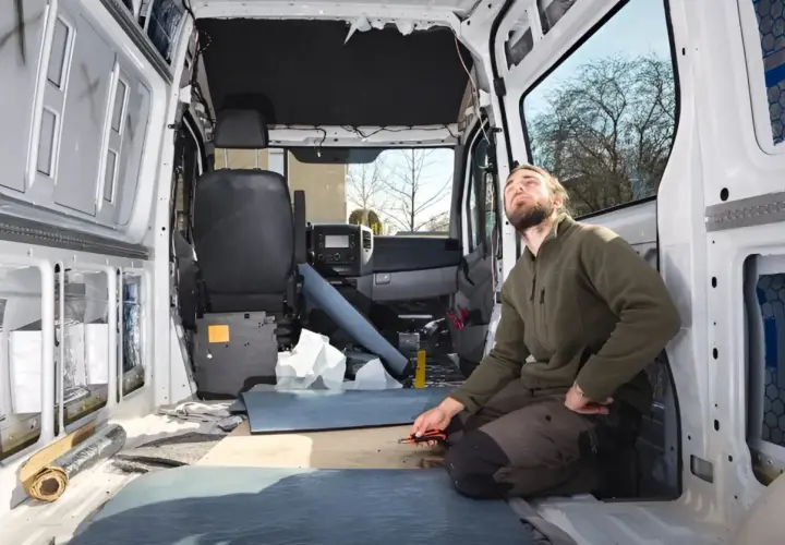 Uomo lavora all'isolamento di un'auto camperizzata. Materiali sparsi, sedili rimossi, pronto per la trasformazione.